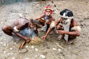Wamena, Indonesia - January 9, 2010: Three men of the Dani tribe in a traditional dress smoking a cigarette in Dugum Dani Village. Baliem Valley Papua, Irian Jaya, Indonesian New Guinea