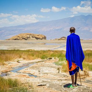 Lake Natron, Tanzania - October 04, 2013: Maasai man is standing at Lake Natron in Tanzania. He looks at the salt lake on the horizon where a herd of giraffes running across the lake.