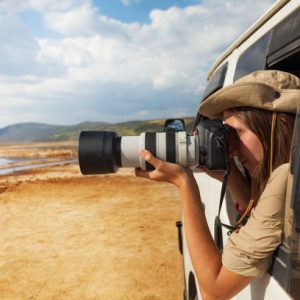 Side view portrait of young woman taking photo of Kenyan lake Nakuru from the open window of safari jeep
