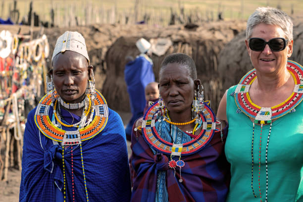 istockphoto-1301076120-612×612 Serengeti, Tanzania - March 12, 2015: Masai with traditional ornaments and tourist review of daily life of local people on March 12, 2015 near Serengeti National Park.